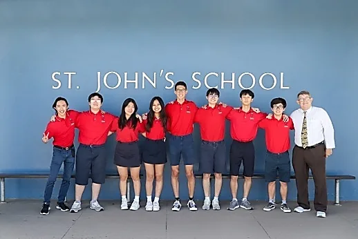 St. John’s School の校名の壁の前に並ぶ生徒たち